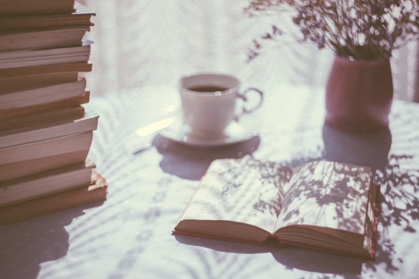 Stack of books with an open book and a cup of coffee